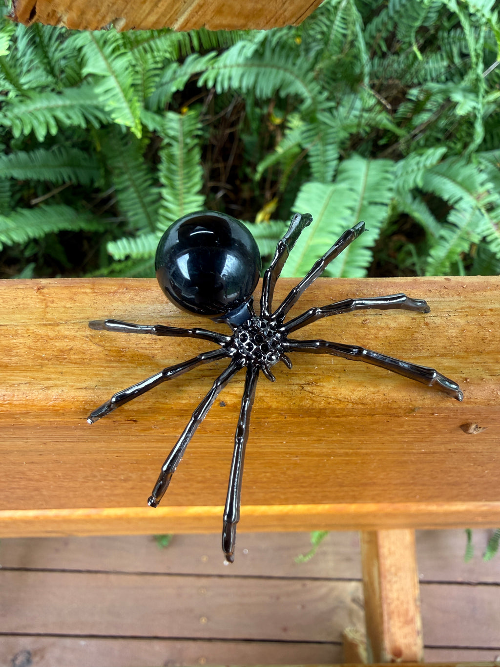 Black obsidian spider decoration on a wooden surface with green foliage in the background