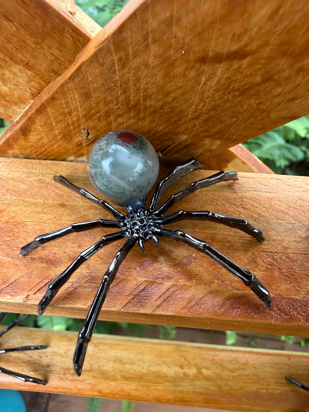 Decorative bloodstone metal spider on a wooden surface with a blurred natural background