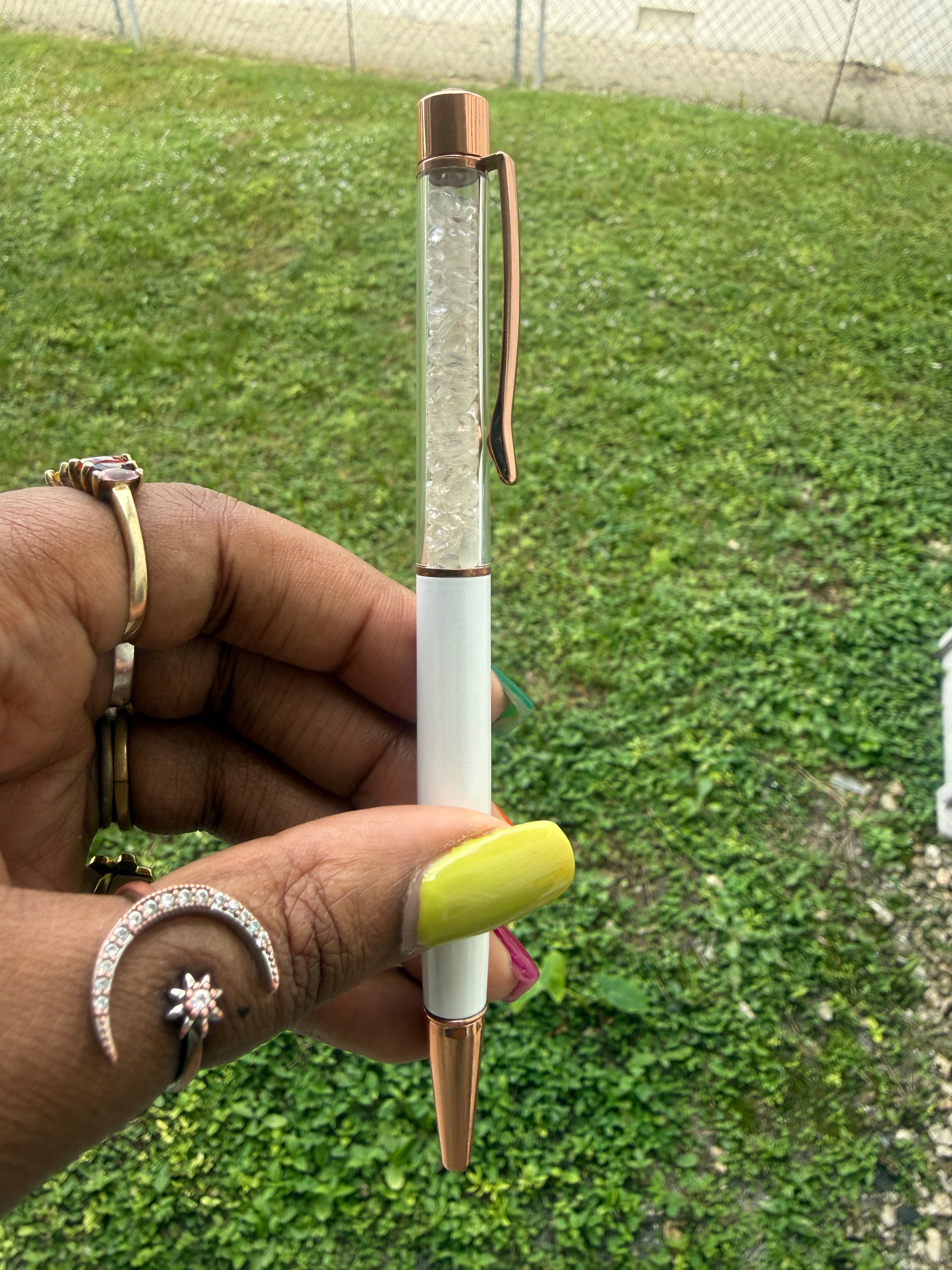 Hand holding a clear Quartz pen with a green grass background