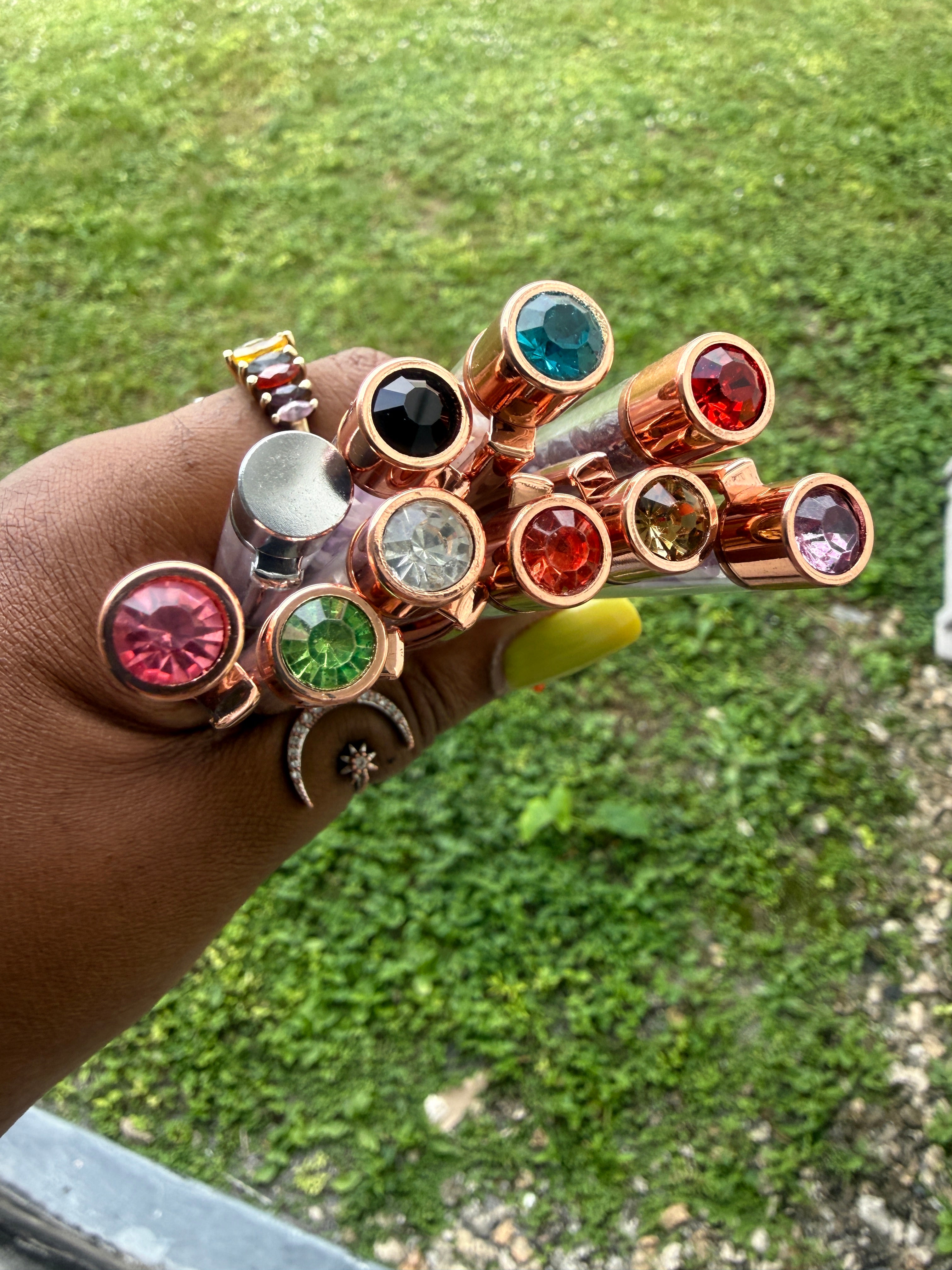 Hand wearing multiple rings with colorful gemstones against a grassy background