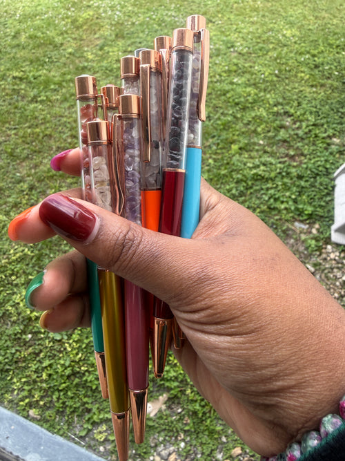 Hand holding a collection of colorful pens against a grassy background