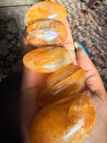 Five polished orange-yellow crystal points held in a person's hand, showing translucent amber tones with natural internal inclusions.