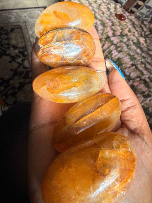 Five polished orange-yellow crystal points held in a person's hand, showing translucent amber tones with natural internal inclusions.
