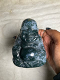 A sculpture of the Buddha made from moss agate, held in a person's hand.