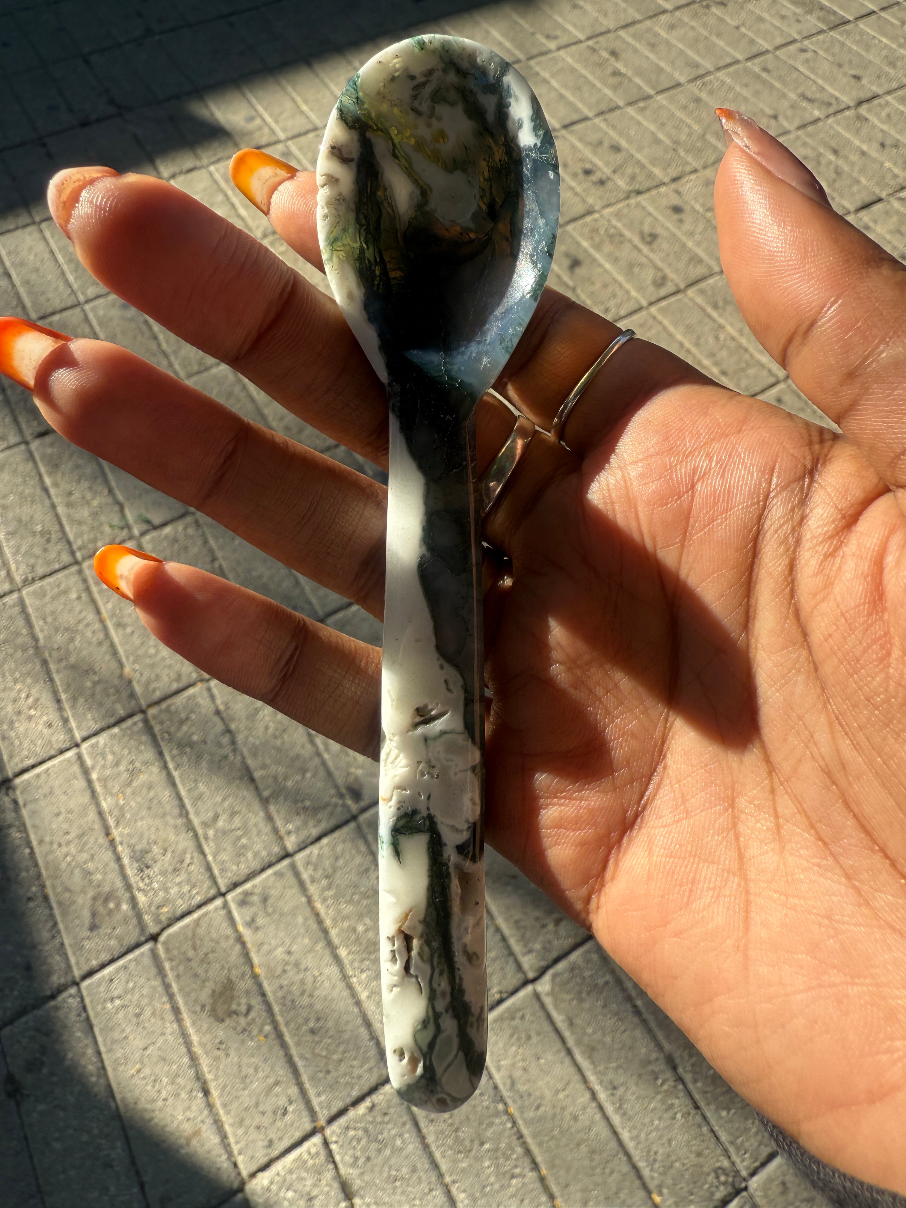 Hand holding a moss agate spoon on a paved surface