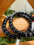 Black beaded bracelets on a wooden stand with a natural background