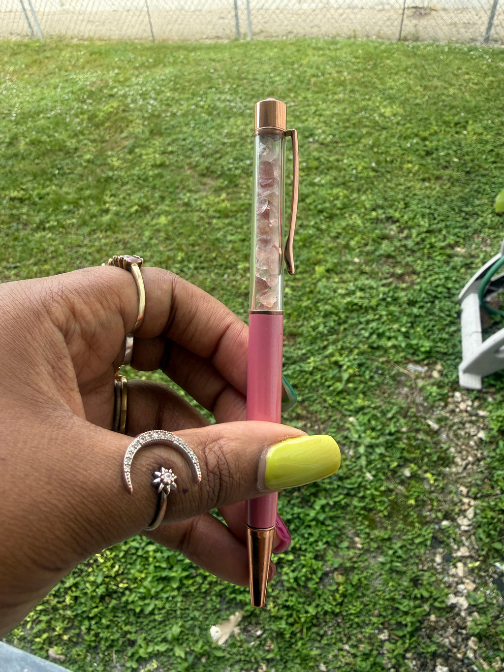Hand holding a rose quartz pen with a green lawn background