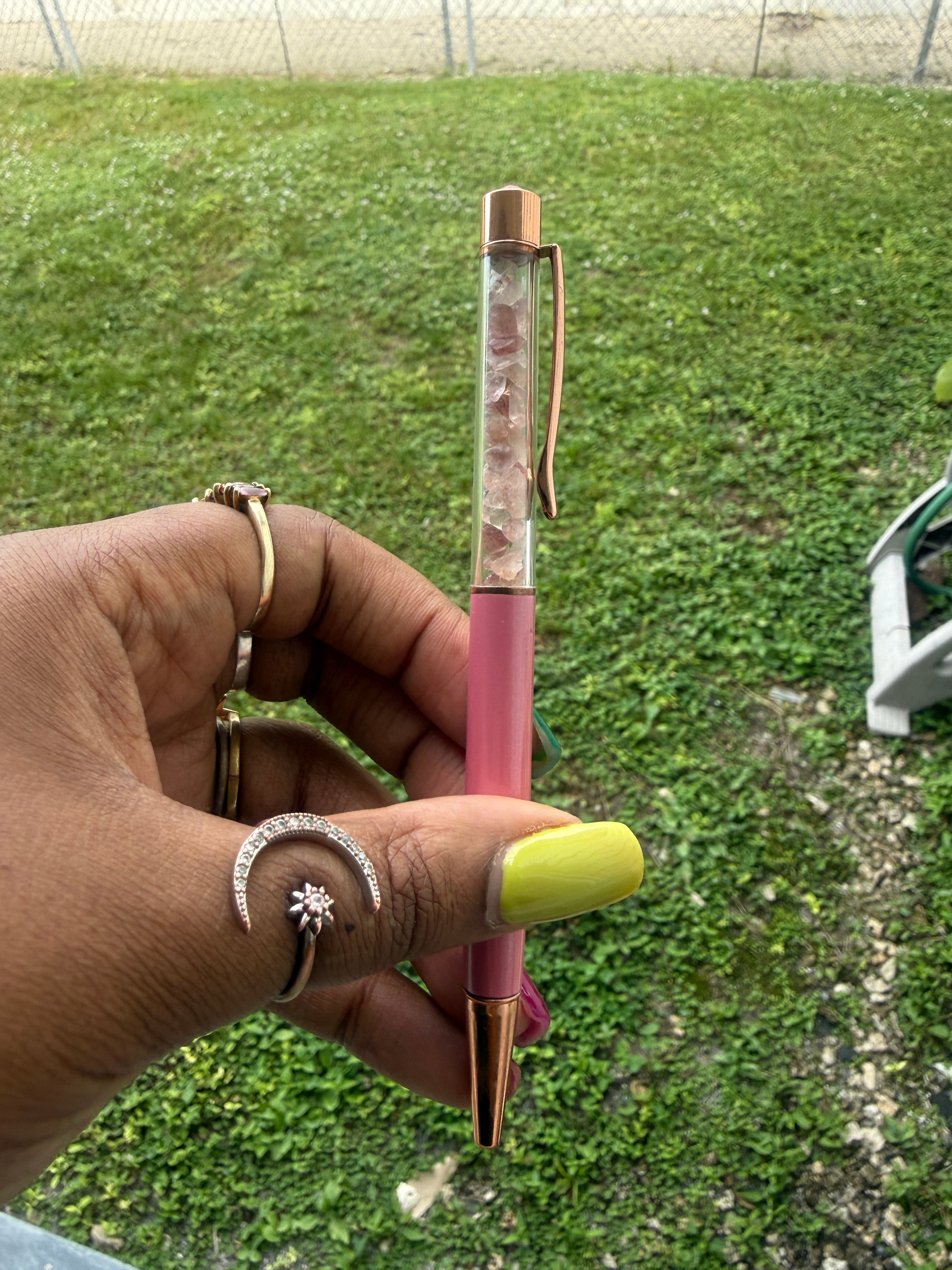 Hand holding a rose quartz pen with a green lawn background